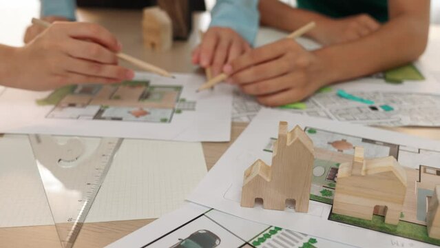 Smart architect and safety engineer discussion about building blueprint on table with architectural document, measurement tools and wooden block scatter around at modern office. Closeup. Delineation.