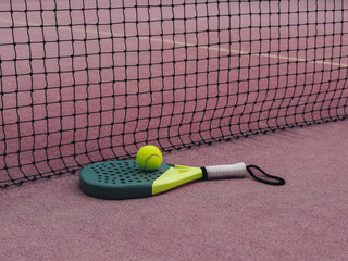 Padel Racket and Yellow Ball on Clay Court by Net on the Floor