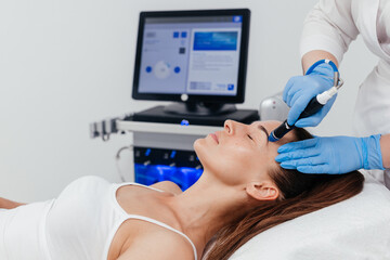 Middle aged beautician holding ultrasound device for hydro facial lifting and skin tightening...