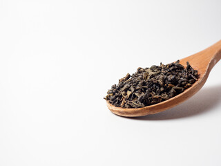 dry black tea leaves in a wooden spoon on a white background. Healthy tonic drink