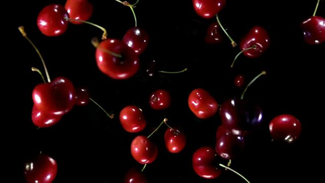 Delicious juicy red cherries are bouncing up and rotating on a black background in slow motion