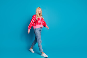 Full size photo of optimistic person dressed knitwear jumper jeans look at sale walk in empty space isolated on blue color background