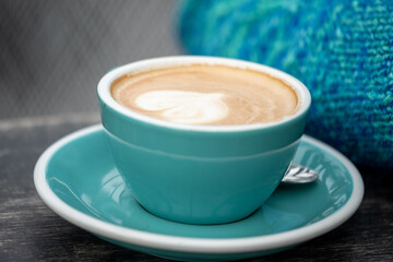 A close up ,blue, steaming cup of latte with artful foam, a heart, in a teal cup, accompanied by a...
