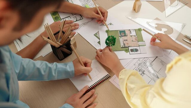 Architect and engineer use tree model discuss about building blueprint on table with architectural document, measurement tools and wooden block scatter around at modern office. Closeup. Delineation.