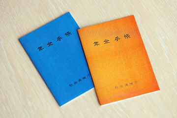 Fototapeta na wymiar Japanese pension insurance booklets on table. Blue and orange pension book for japan pensioners close up