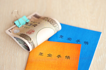 Japanese pension insurance booklets on table with yen money bills. Blue and orange books for japan...