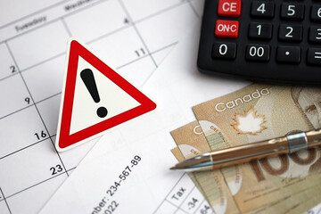 Attention sign and calculation results in schedules lies on table with canadian money bills,...