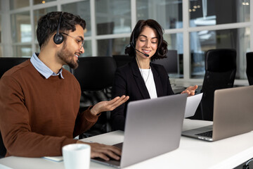 Handsome young businessman and beautiful business woman in headsets using laptops