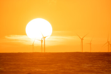 Wind turbine on the sea during sunset. Renewable energy sources. Technology and production. Seascape. Electric generator. Bright sun during sunset.