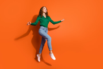 Full length photo of girly dreamy lady dressed green shirt jumping high running emtpy space isolated orange color background