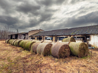 Round bale of hay by old dirty abandoned farm building with broken windows. Dark dramatic sky....
