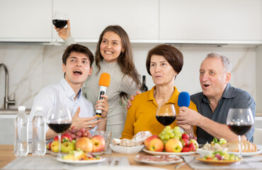 Young couple and parents meeting at home have fun at festive table in big kitchen, sing excited...