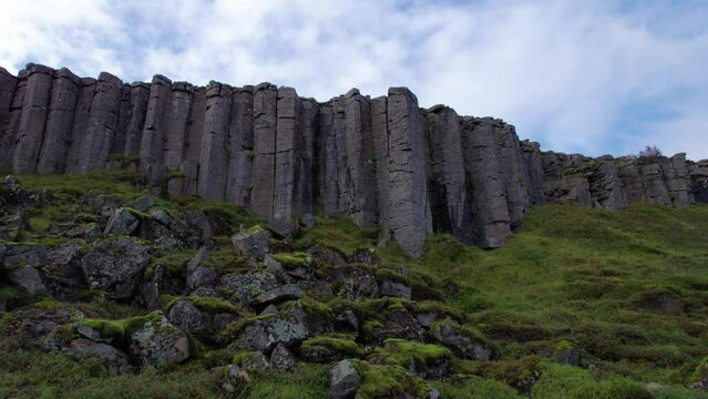 Low Angle Drone Gerduberg Cliffs Iceland Aerial Slow Backwards Reveal Landscape Row of Hexagonal Basalt Columns. Wall of Rock Columns and Green Grass Cloudy Sky. 4K High Quality Color Corrected.