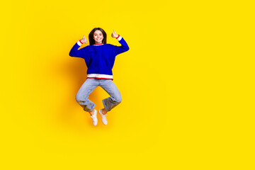 Full length photo of pretty teen girl jumping thumb up wear trendy knitwear blue outfit isolated on yellow color background
