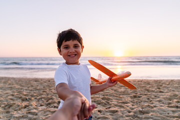 Smiling child extends toy airplane at the beach