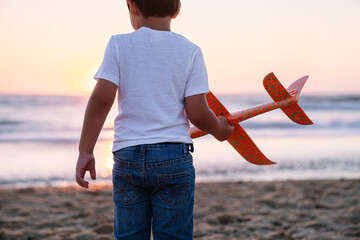 Child gazes at sea with airplane in hand at dusk.