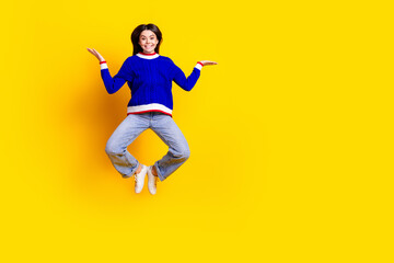 Full length photo of pretty teen girl jumping hold empty space wear trendy knitwear blue outfit isolated on yellow color background