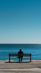 Naklejka na ściany i meble studio shot of A lone figure sitting quietly on a bench by the sea, realistic travel photography, copy space for writing