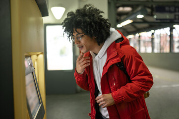 Curly-haired guy standing near ATM and looking at it