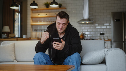 Man sitting on couch using smartphone check message read notice receive good news on e-mail...
