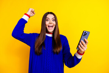 Photo portrait of pretty teen girl hold gadget winning wear trendy knitwear blue outfit isolated on yellow color background
