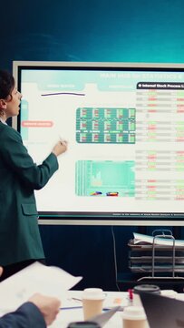 Team of business colleagues reviewing statistics and sales data on interactive board, working together on supply chain management strategies. Startup coworkers discuss industry changes. Camera B.