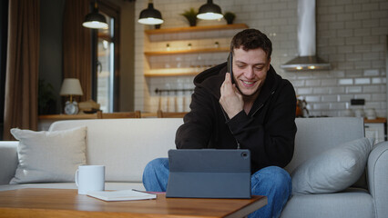 Smiling man sitting on the sofa at home enters credit card number into the tablet computer to shop...