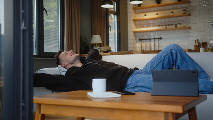 Happy man falls down lie on comfortable sofa enjoying rest relaxation after hard day at work makes...