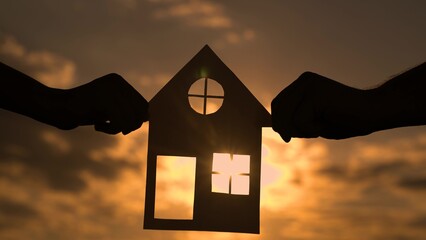 Family Home, Real estate insurance. Familys hands are holding paper house at sunset, sun is shining through window. Symbol of house, happiness. Concept of building house for family. Dream to buy house - Powered by Adobe