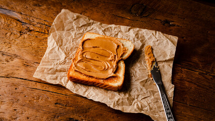 Peanut butter on toasted bread placed on a parchment paper with wooden background. Selective focus.