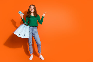Photo of funky pretty lady dressed green shirt holding shoppers writing device pointing emtpy space isolated orange color background