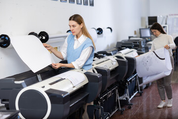 Caucasian woman working in printing office, using large format printer.
