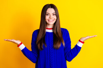 Photo portrait of pretty teen girl hold compare empty space wear trendy knitwear blue outfit isolated on yellow color background