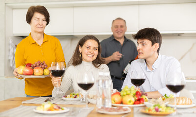Smiling young guy with girlfriend visiting parents. Young couple sitting with glasses of wine at...