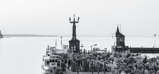 Schwarz-Weiss Aufnahme des Hafens mit Imperia-Statue, dem Bodensee mit Katamaran Fähre und...