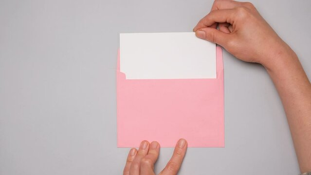 A hand pulls out a white card from a bright pink envelope. Top view of a pink envelope on gray background. Banner for social media ad with copy space.