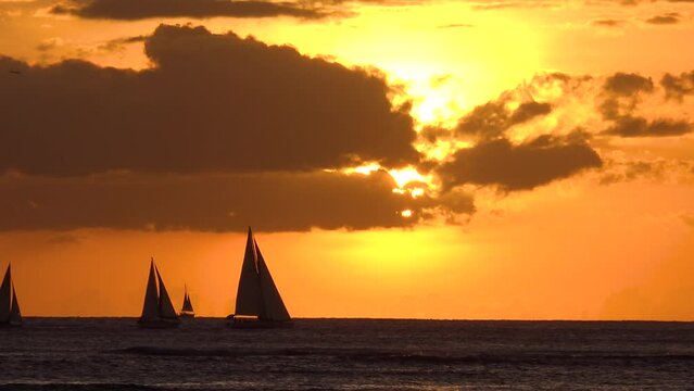 HAWAII - 3.19.2024 - Sailboats move off the coast of Hawaii at sunset.