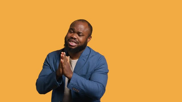 African american man putting hands together in begging gesture, making wish, isolated over yellow studio background. BIPOC person asking for something, praying and hoping, camera A