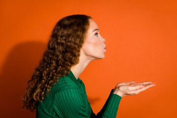 Photo of positive flirty lady dressed green shirt sending arms kiss emtpy space isolated orange color background