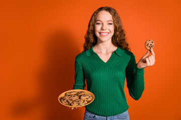 Photo of dreamy cute lady dressed green shirt enjoying biscuits empty space isolated orange color background