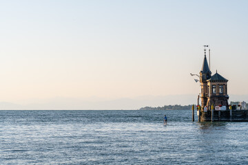 Tourist auf Standup Paddle färht an Leuchtturm und Hafeneinfahrt mit der Konstanzer Fahne vorbei....