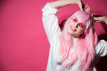 Close-up portrait of a young woman with braces in a pink wig and sunglasses on a pink background. Copy space. 