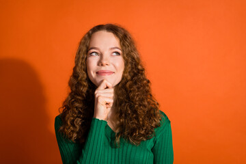 Photo of happy dreamy lady dressed green shirt hand chin looking emtpy space isolated orange color background