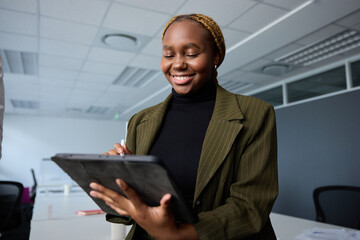 Young businesswoman in businesswear smiling while using digital tablet and digitized pen in office