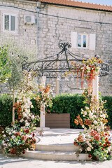 Fototapeta na wymiar Wedding rotunda arch decorated with flowers stands in the courtyard of an ancient stone house