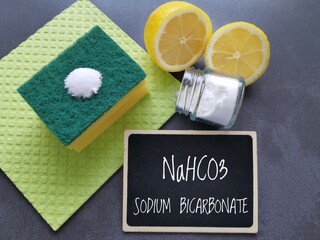 Sodium bicarbonate powder in glass jar, lemon and sponge with chemical formula of sodium bicarbonate. Eco friendly natural cleaner, baking soda and lemon for cleaning home or removing stains.