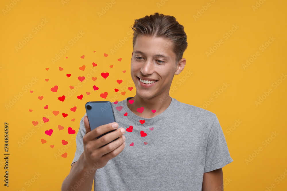 Wall mural Long distance love. Man chatting with sweetheart via smartphone on golden background. Hearts flying out of device