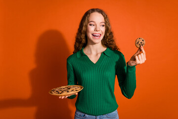 Photo of pretty hungry lady dressed green shirt stick out eating cookies empty space isolated orange color background