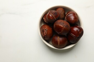 Obraz premium Roasted edible sweet chestnuts in bowl on white marble table, top view. Space for text