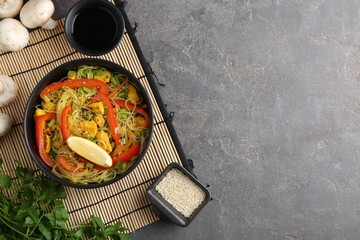 Stir-fry. Delicious cooked noodles with chicken and vegetables in bowl served on gray textured table, flat lay. Space for text